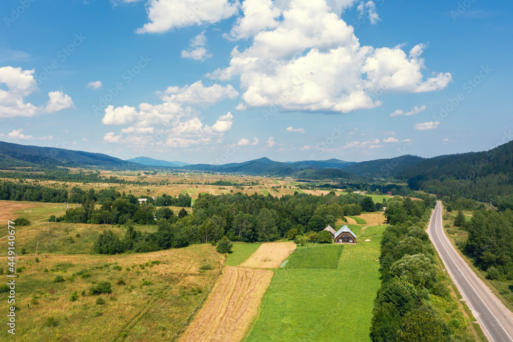 Obraz premium Aerial view of a mountain valley. Rural landscape in summer. View of the village, highway, and mountains on a sunny day