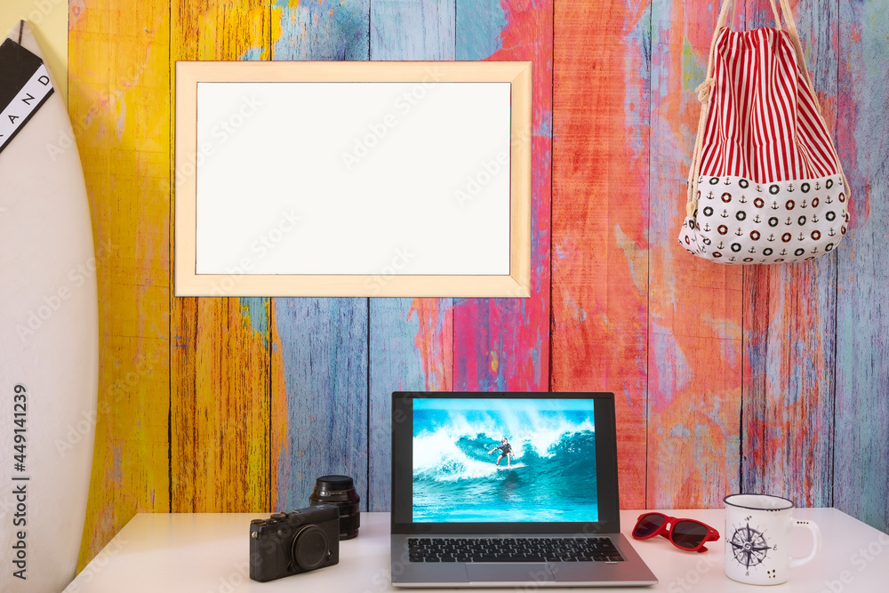 Obraz premium Desktop with laptop computer and photograph of a young surfer. Concept of summer and beach holidays