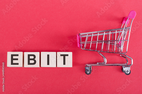 The word EBIT, on wooden cubes, on a pink background with a shopping trolley.