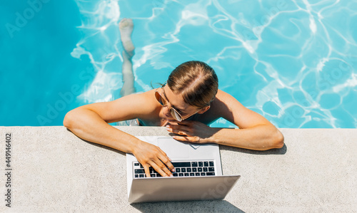 Attractive young woman in sunglasses, uses laptop and work remotely over the pool, Attractive woman smiling, using laptop in the pool