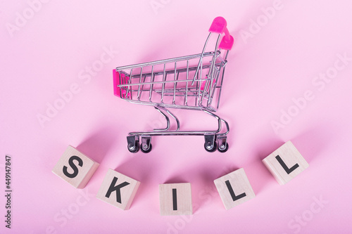 SKILL - word on wooden cubes, on a pink background with a shopping trolley.