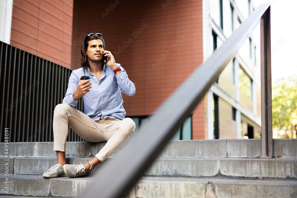 Young man sitting on the stairs drinking coffee. Handsome businessman using the phone while drinking coffee. Young man sitting on the stairs drinking coffee. Handsome businessman using the phone while drinking coffee.