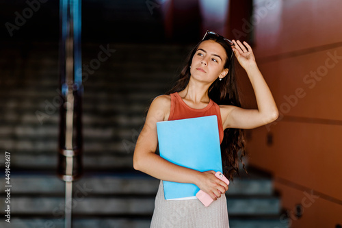 Portrait of a student girl with a folder in her hand  adjusting her glasses  going to class