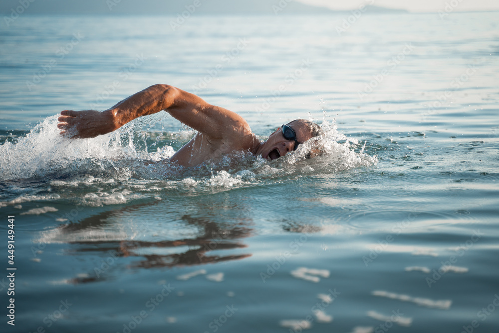 A sports man is engaged in swimming on the sea. Swims crawl across the ocean at dawn