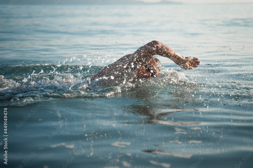 Fototapeta premium A sports man is engaged in swimming on the sea. Swims crawl across the ocean at dawn