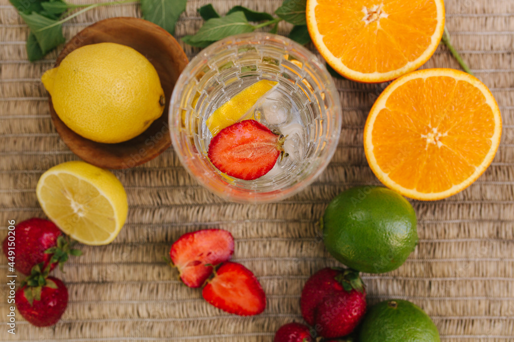 Top view of a tall glass with water ice and strawberry. Slices fresh fruits on the table outdoor. Lime lemon and orange. Food concept. Close up Top view of a tall glass with water ice and strawberry. Slices fresh fruits on the table outdoor. Lime lemon and orange. Food concept. Close up