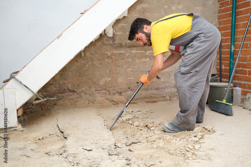Young builder breaking up a house floor with a crowbar. Young builder breaking up a house floor with a crowbar.