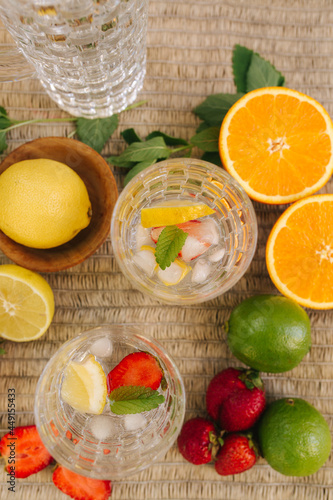 Top view of two tall glasses with water ice and strawberry. Slices fresh fruits on the table outdoor. Lime lemon and orange. Food concept