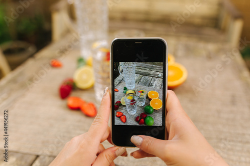 Female hand hold phone and make photo of table with fresh citrus and strawberry. Woman make photo for social network