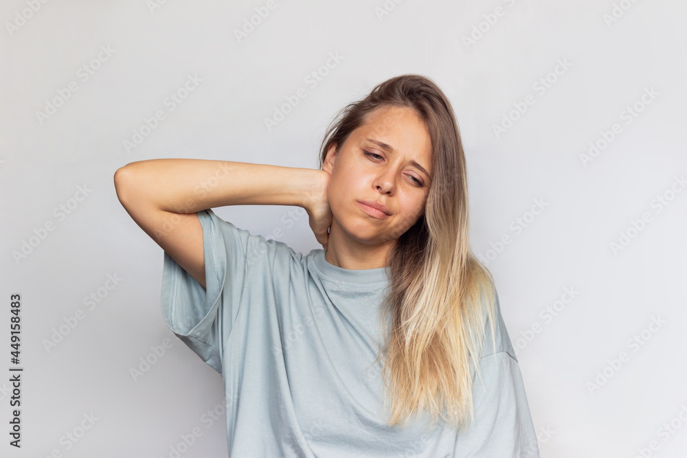 A young beautiful blonde woman with a neck pain holding her neck isolated on gray background. The girl suffers from an osteochondrosis A young beautiful blonde woman with a neck pain holding her neck isolated on gray background. The girl suffers from an osteochondrosis