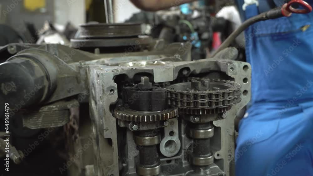 View of disassembled car engine. hands of professional mechanic in blue uniform, repairing engine. repairman working in garage or workshop. person who is engaged in servicing cars or motorcycles. View of disassembled car engine. hands of professional mechanic in blue uniform, repairing engine. repairman working in garage or workshop. person who is engaged in servicing cars or motorcycles.