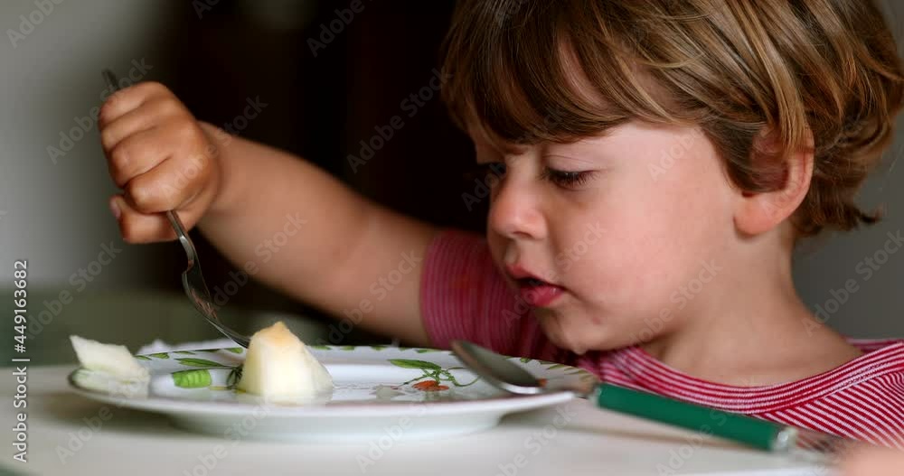 Little boy using fork eating melon fruit. Child eating healthy food Little boy using fork eating melon fruit. Child eating healthy food