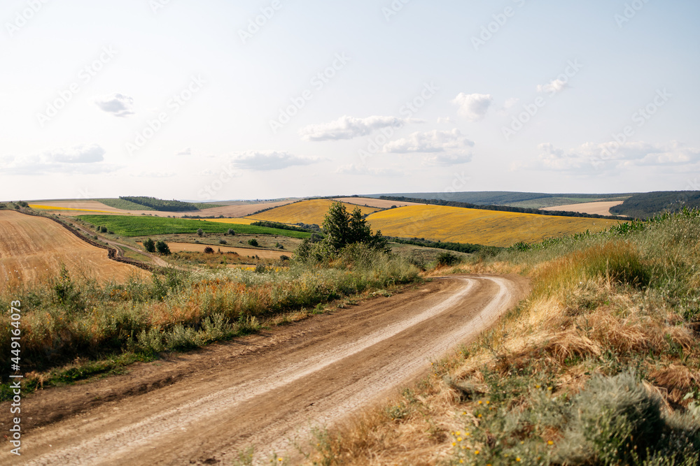 Countryside road going through beautiful fields and hills. View from high altitude. Outdoors, evening golden hour landscape view. Photo.