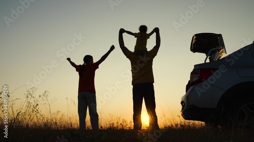 Happy family travels by car. Parents and children stopped at campsite by car. Dad with child, daughter on his shoulders, mom, children dance and admire beautiful sunset. Travel by car. Healthy family