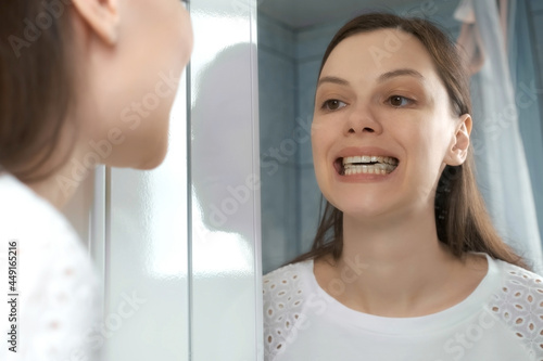Young woman is installing splint for down teeth to correct the bite looking at mirror in bathroom. Inserting aligners on down teeth for correcting jaw joints. Dentistry treatment. photo