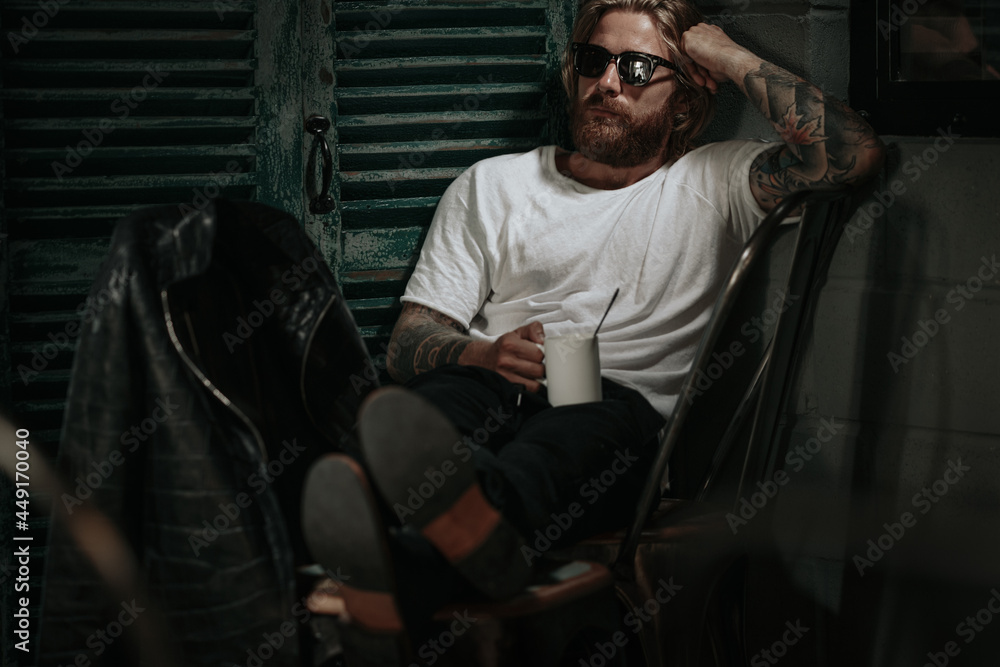Brutal caucasian hipster holding glass of drink looking to window 