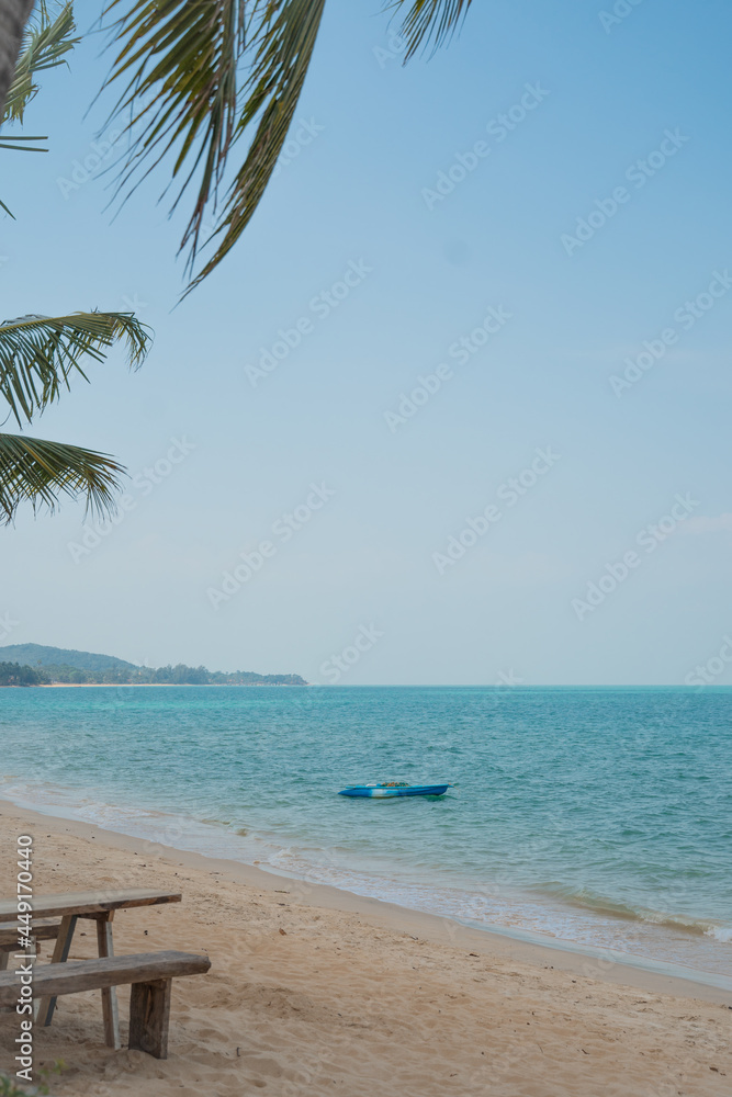 A white boat is anchored and floats on the waves in a beautiful calm sea near the shore of a sandy beach
