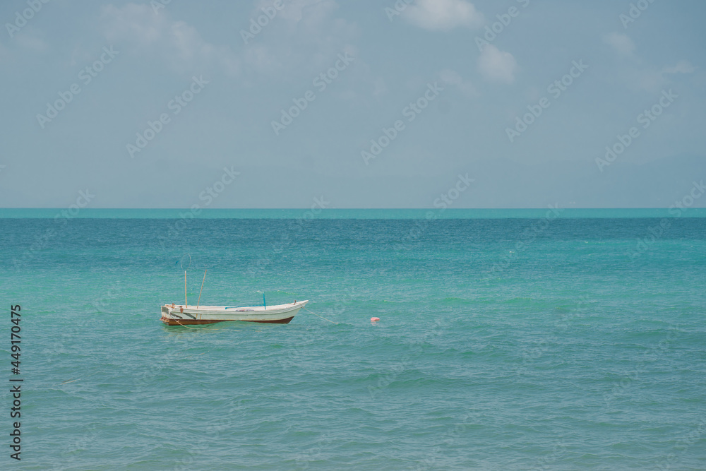 A white boat is anchored and floats on the waves in a beautiful calm sea near the shore of a sandy beach