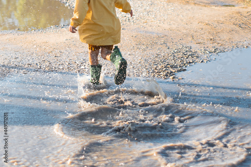Happy boy in yellow jacket and green wellington boots jump and walk after rain