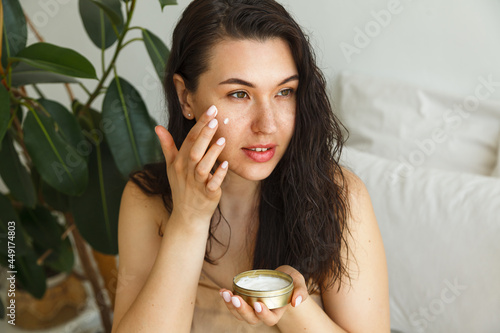 Young attractive woman applying face cream in the bedroom