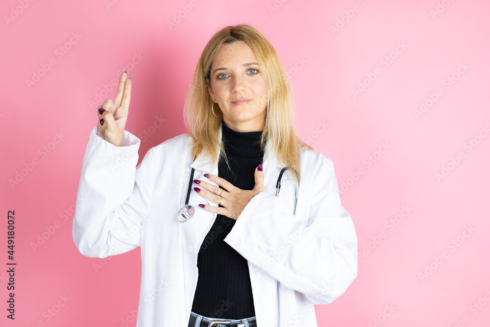 Young blonde doctor woman wearing stethoscope standing over isolated pink background smiling swearing with hand on chest and fingers up, making a loyalty promise oath Young blonde doctor woman wearing stethoscope standing over isolated pink background smiling swearing with hand on chest and fingers up, making a loyalty promise oath