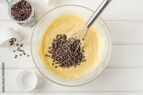 Muffin dough with chocolate chips in a bowl on a white wooden background. Recipe step by step. Top view.