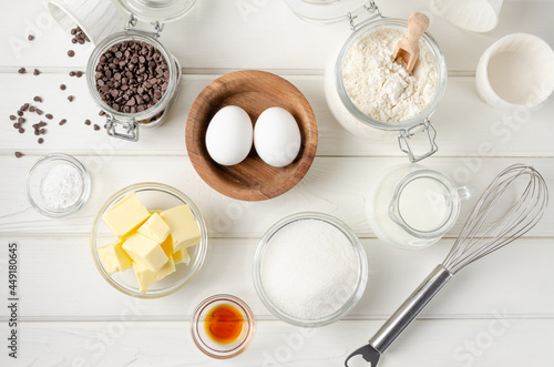 Ingredients for making muffins with chocolate chips. Eggs, butter, sugar, flour, vanilla, chocolate chips on a white wooden background. Recipe step by step. Top view.