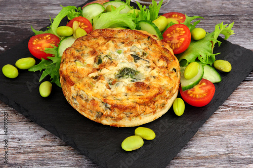 Spinach and kale quiche with fresh salad and edamame beans on a slate serving board