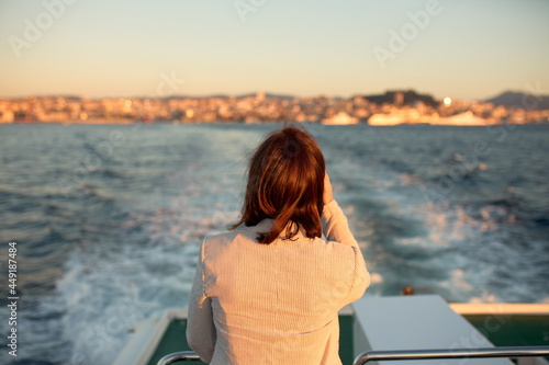 Woman with her back on the back of a boat watching as it moves away from the port of the city.