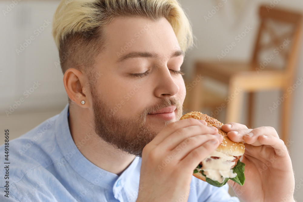 Young man eating vegan burger in kitchen Young man eating vegan burger in kitchen