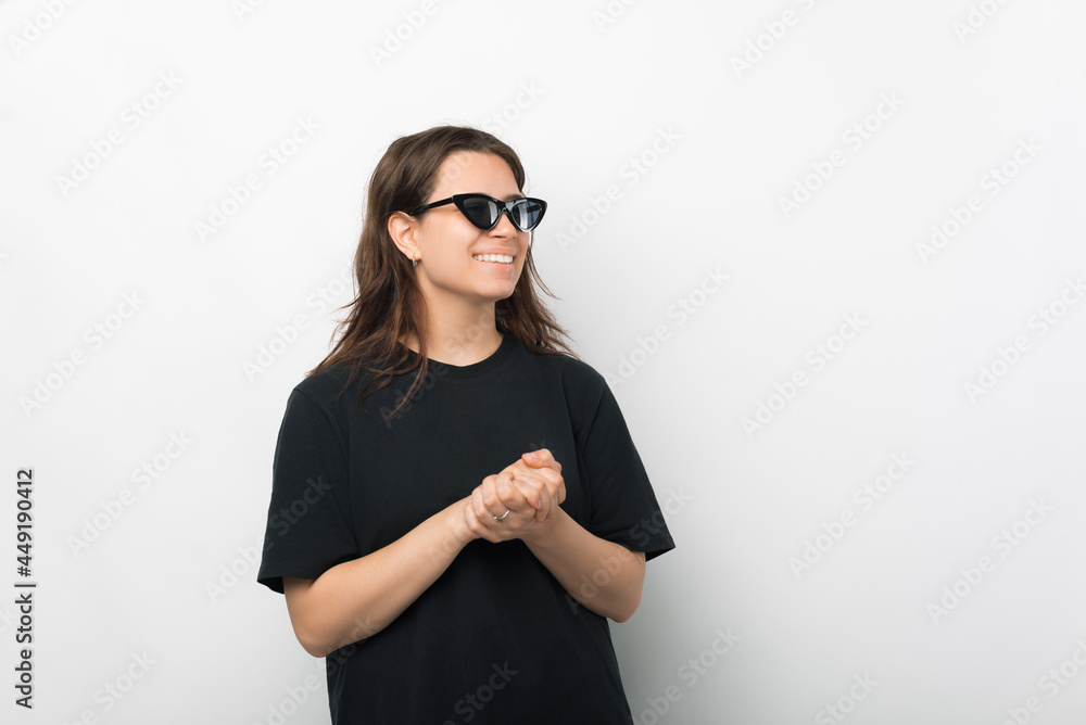 Young woman wearing black tshirt and sunglasses, having conversetion with someone and standing with hands together Young woman wearing black tshirt and sunglasses, having conversetion with someone and standing with hands together