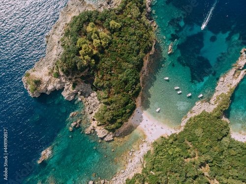 Aerial view of Corfu island. White boats float in turquoise water near the shore. Heart shaped island. Top down view.