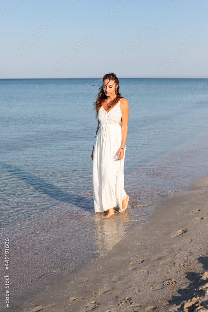 A young girl in a white sundress is walking along the seashore. A young girl in a white sundress is walking along the seashore.