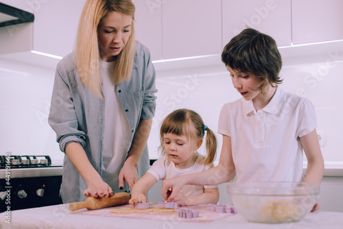 Little girl makes dough figurines with her mother and older sister in the kitchen.