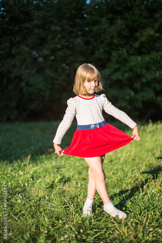 A little girl in a red skirt is dancing on a summer green meadow. A little girl in a red skirt is dancing on a summer green meadow.