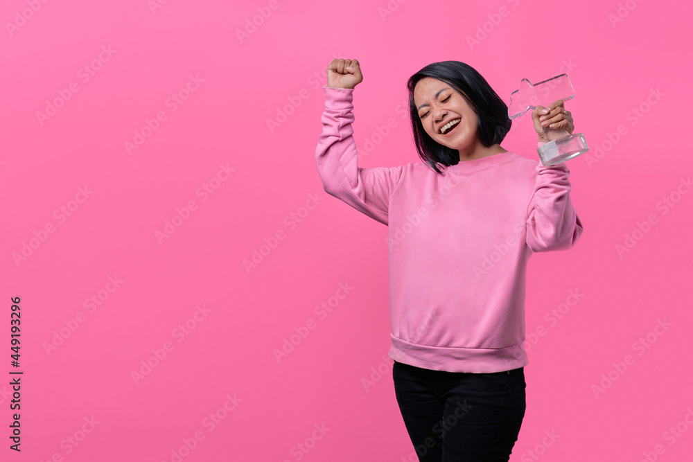 Young woman holding an award statuette receiving a pleasant surprise, excited and raising hands Young woman holding an award statuette receiving a pleasant surprise, excited and raising hands