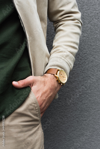 cropped view of young man with stylish wristwatch posing with hand in pocket near grey wall