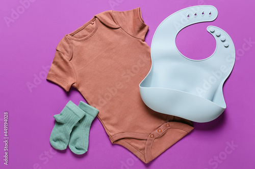 Baby clothes and bib on color background photo