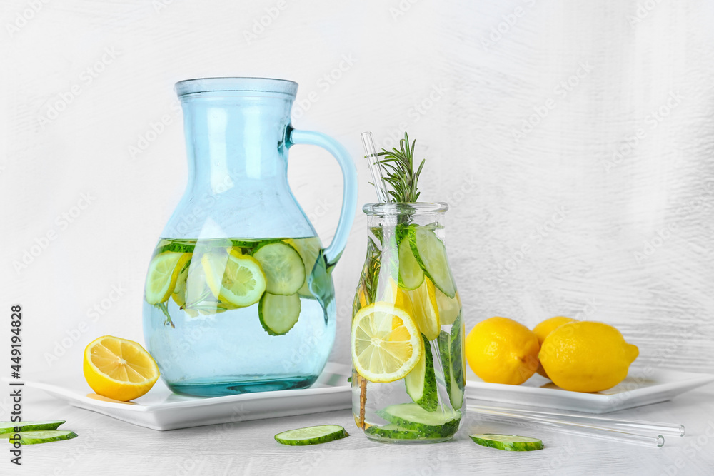Bottle and jug with cucumber lemonade on light background Bottle and jug with cucumber lemonade on light background