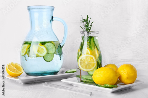Bottle and jug with cucumber lemonade on light background
