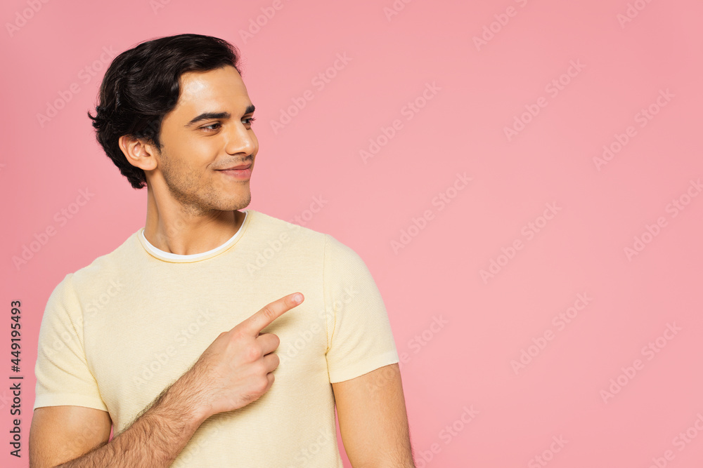 joyful young man pointing with finger and looking away isolated on pink joyful young man pointing with finger and looking away isolated on pink
