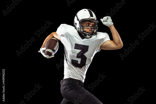 Close-up portrait of American football player playing in sports equipment, helmet and gloves isolated on dark studio background. Concept of sport, competition