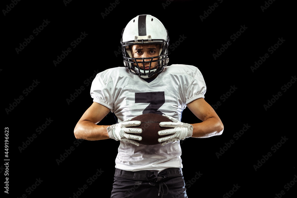 Close-up portrait of American football player in sports equipment, helmet and gloves isolated on dark studio background. Concept of sport, competition Close-up portrait of American football player in sports equipment, helmet and gloves isolated on dark studio background. Concept of sport, competition