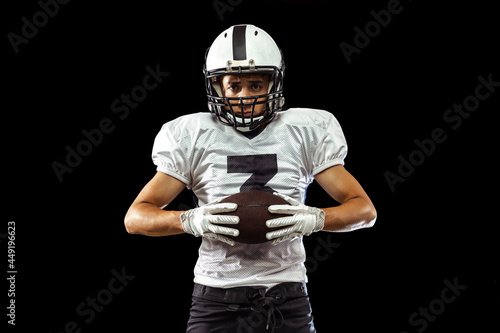 Close-up portrait of American football player in sports equipment, helmet and gloves isolated on dark studio background. Concept of sport, competition