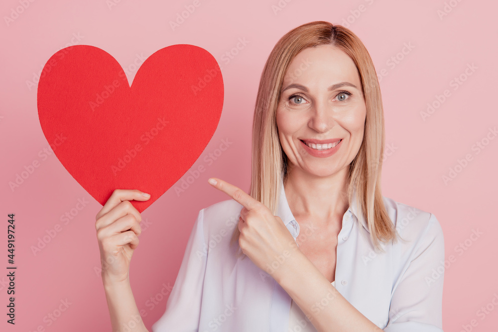 Photo of young woman point finger big heart valentine day choice advert isolated over pink background Photo of young woman point finger big heart valentine day choice advert isolated over pink background