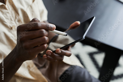 Close-up of African man holding pen and typing on touch screen of digital tablet during his online work