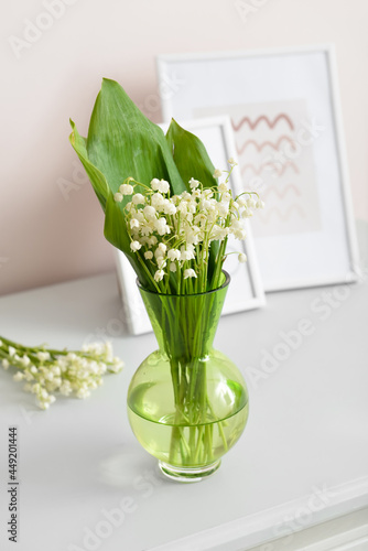 Vase with lily-of-the-valley flowers and pictures on shelf