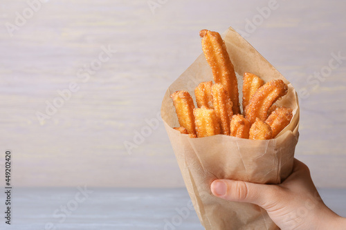 Female hand with tasty churros in parchment on light wooden background, closeup