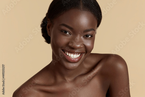 Portrait close up of beautiful african girl. Smiling young woman looking at camera. Concept of skincare. Isolated on beige background. Studio shoot