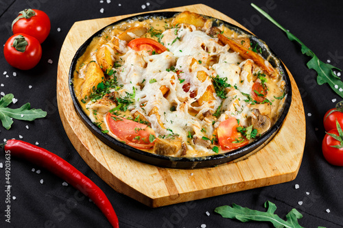baked vegetables with cheese and mushrooms in a frying pan on a wooden stand on a dark background with ingredients